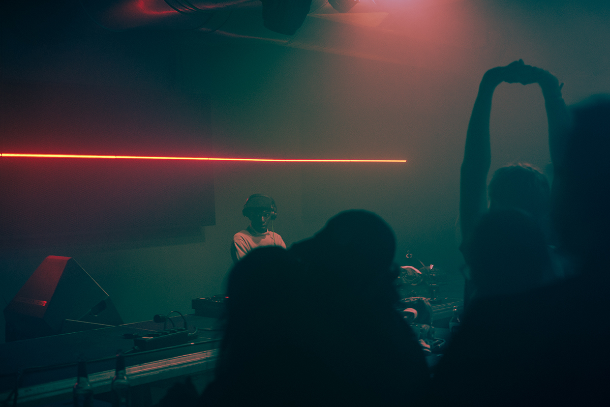 a dj is performing during an event, silhouettes of the audience are visible 